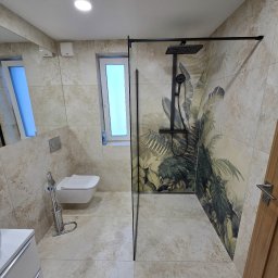 Nowoczesna łazienka z kabiną typu walk-in, beżowymi płytkami imitującymi kamień i akcentem tropikalnej tapety za prysznicem. Minimalistyczna toaleta pod oknem.