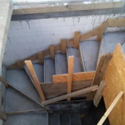 Betonowe schody w trakcie budowy z drewnianym szalunkiem, widok z góry. Elementy konstrukcyjne i surowy beton w szarej tonacji.