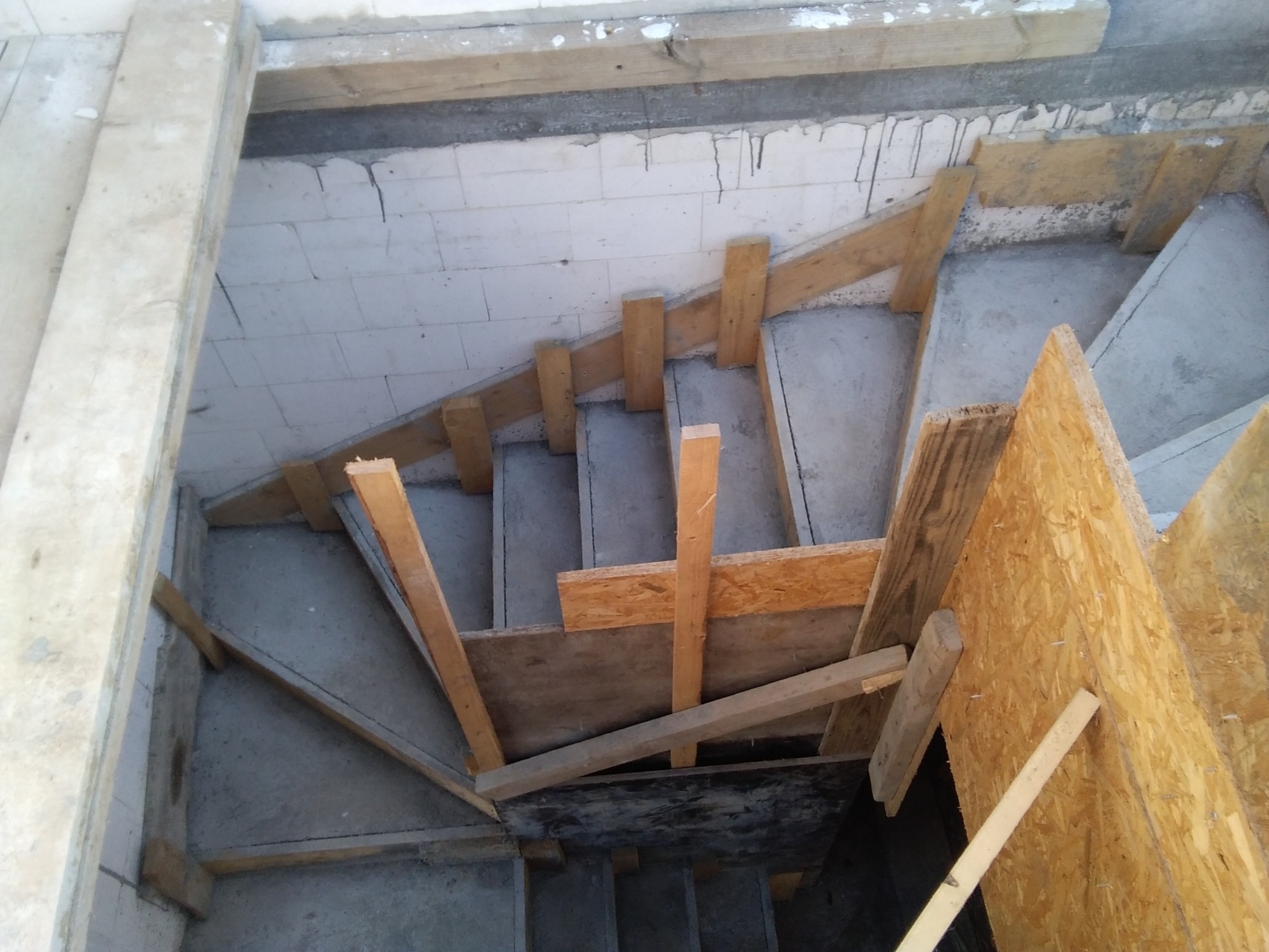 Betonowe schody w trakcie budowy z drewnianym szalunkiem, widok z góry. Elementy konstrukcyjne i surowy beton w szarej tonacji.