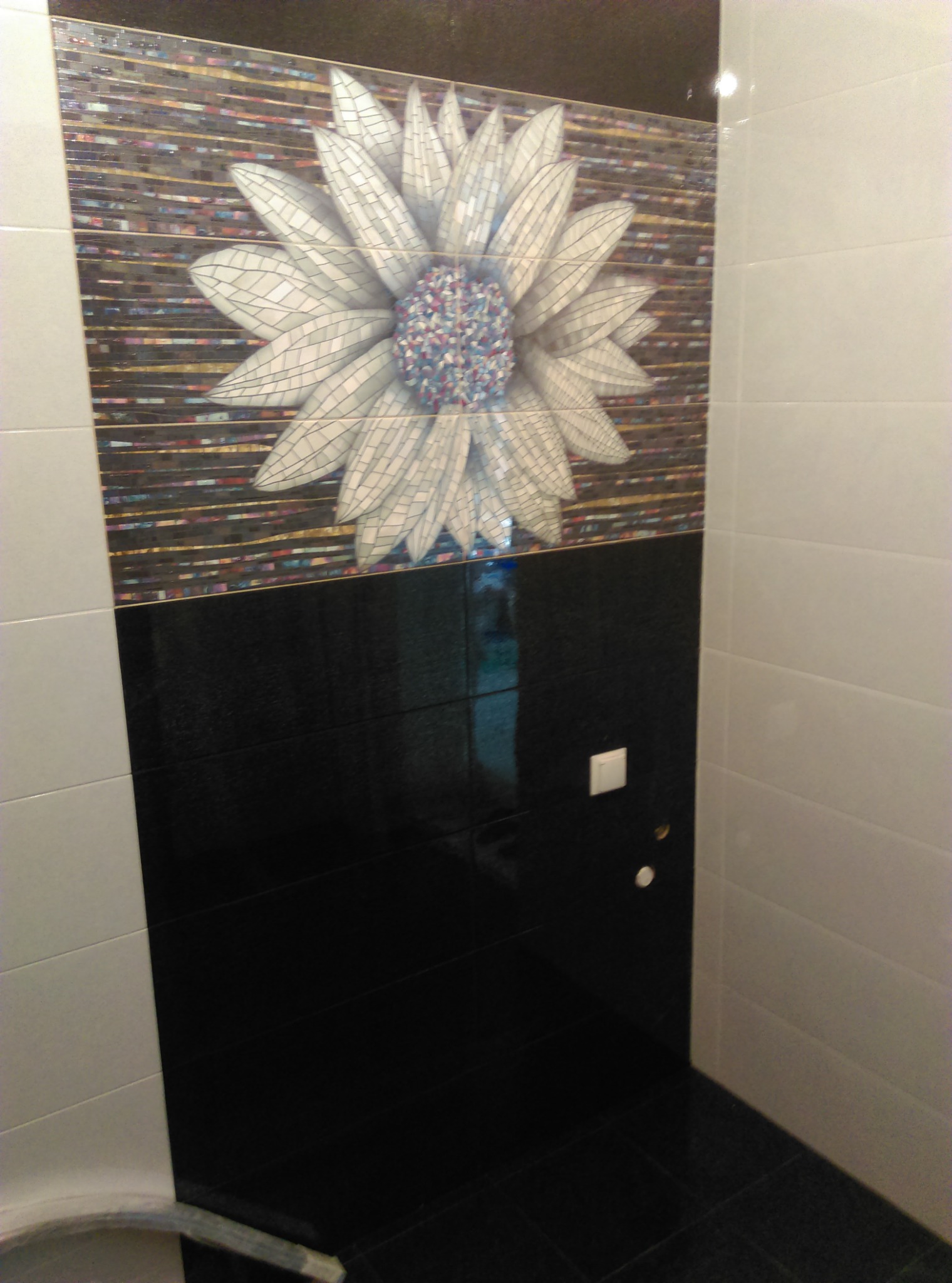 Wykończona łazienka z czarno-białymi płytkami i dekoracyjnym motywem kwiatowym z mozaiki nad czarną częścią ściany.