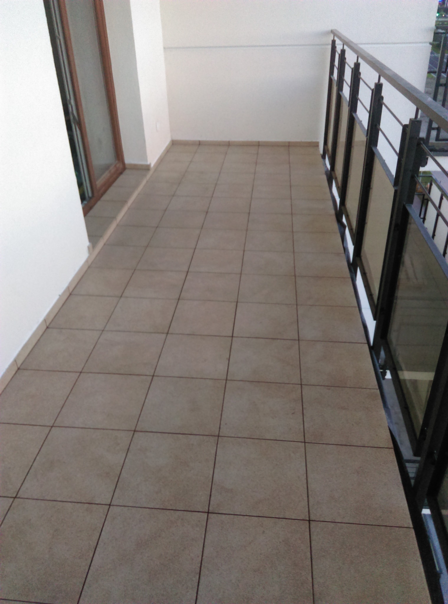 Wyłożony jasnymi płytkami balkon w Olsztynie z metalową balustradą i widokiem na zewnątrz.