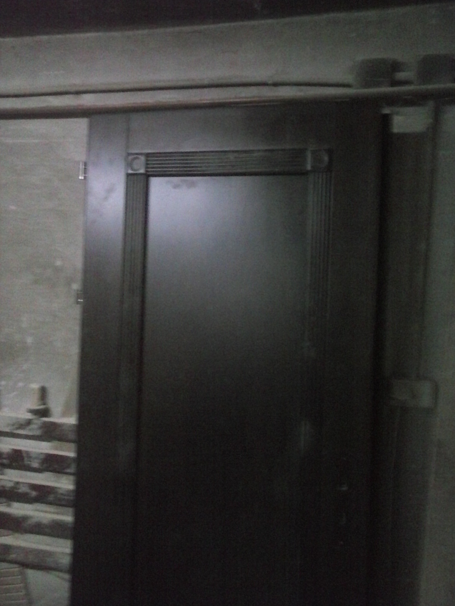 Ciemne drzwi przesuwne z dekoracyjnym obramowaniem, zamontowane na szynie w surowym wnętrzu.