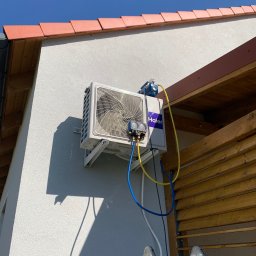Klimatyczna Sfera Sp. z o.o. - Zewnętrzna jednostka klimatyzacji Haier zamontowana na ścianie domu, podłączona do pompy próżniowej i manometrów serwisowych, widoczna drabina.