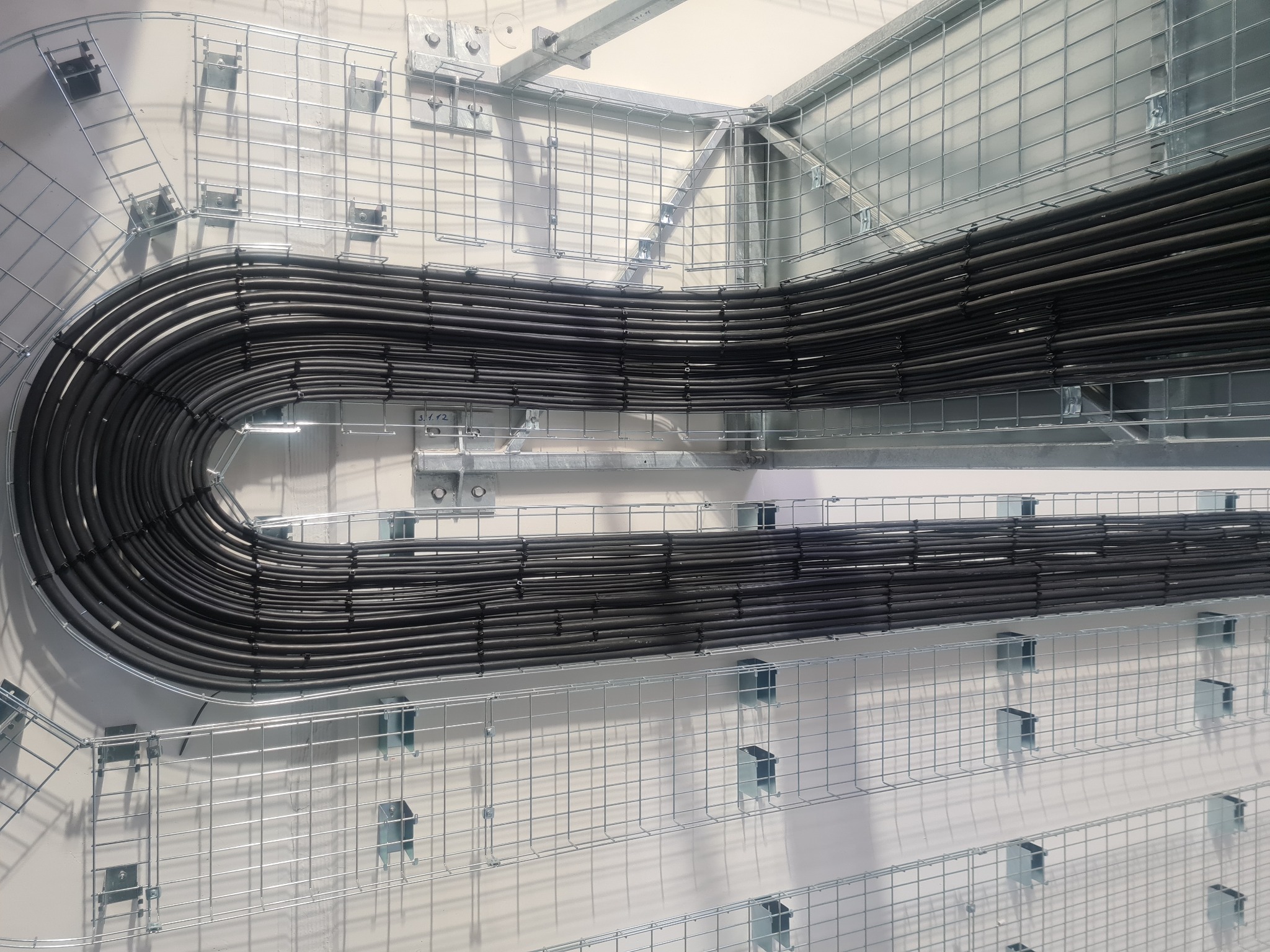 Ułożone równolegle przewody elektryczne w metalowych korytkach kablowych, zamontowane na ścianie, widok z góry, realizacja we Wrocławiu.