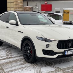 DIAMOND SHINE - Biały samochód Maserati Levante z czarnymi felgami i przyciemnionymi szybami, zaparkowany na śniegu przed budynkiem magazynowym.