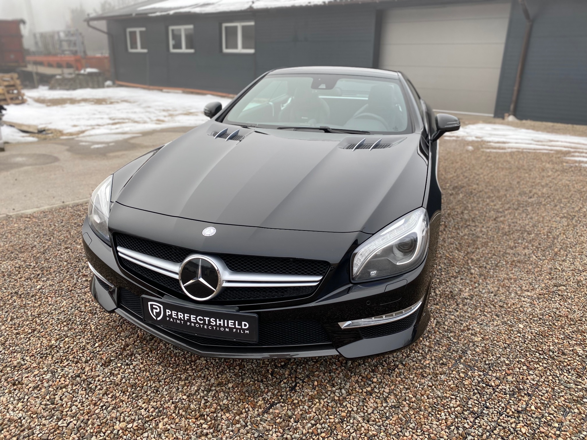 Czarny Mercedes SL z folią ochronną PerfectShield na tle szarego budynku z elementami śniegu na żwirowym podłożu.