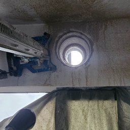 M.S INSTAL-MAT Usługi Hydrauliczne - Wiercenie otworu w stropie za pomocą wiertnicy diamentowej. Widoczne ślady po wierceniu i osłona zabezpieczająca. Praca w toku, widok z dołu.