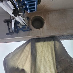 M.S INSTAL-MAT Usługi Hydrauliczne - Wiercenie otworu w suficie za pomocą wiertnicy diamentowej, zabezpieczone płachtą. Widoczne ślady po wierceniu. Sprzęt w kolorze niebieskim.