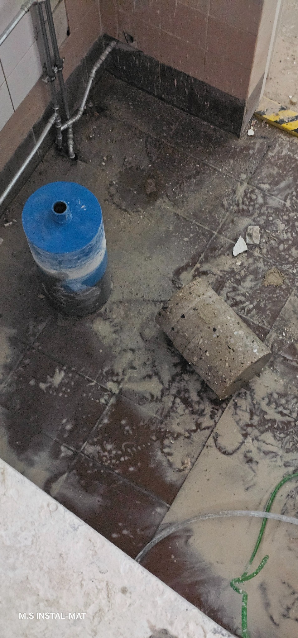 Wykonanie otworu w podłodze pod instalacje. Widoczna wiertnica diamentowa i wycięty rdzeń. Prace hydrauliczne w trakcie realizacji, widoczne rury instalacyjne.