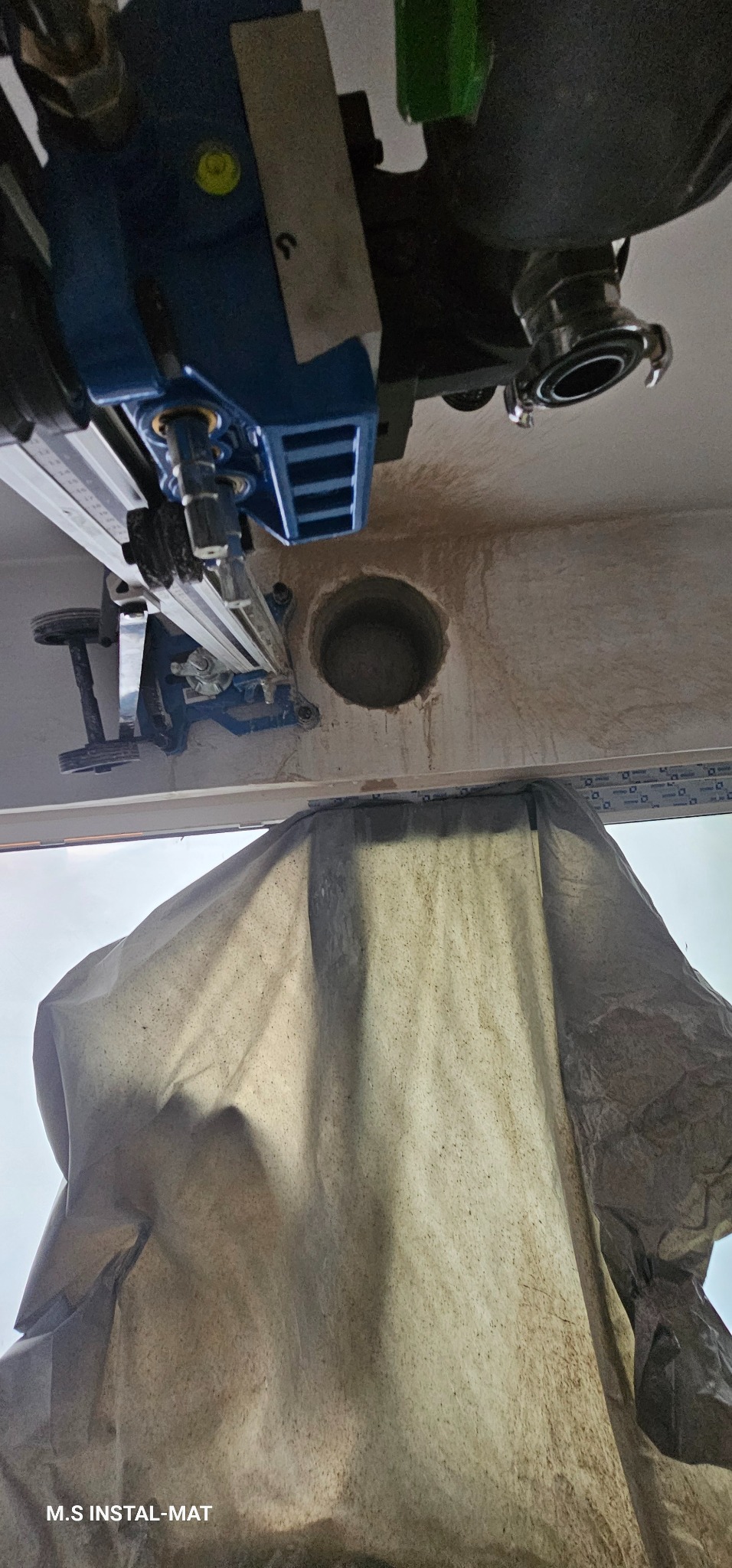 Wiercenie otworu w suficie za pomocą wiertnicy diamentowej, zabezpieczone płachtą. Widoczne ślady po wierceniu. Sprzęt w kolorze niebieskim.