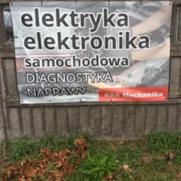 Baner reklamowy na betonowym ogrodzeniu, informujący o usługach: elektryka, elektronika samochodowa, diagnostyka, naprawy, z logo ESA Mechanika.