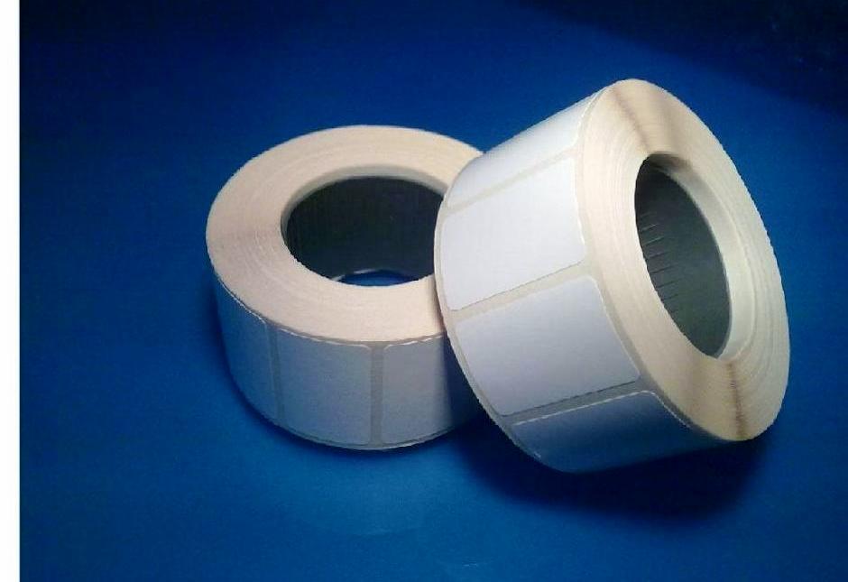 Dwie rolki białych etykiet samoprzylepnych na niebieskim tle, widoczne pojedyncze prostokątne etykiety na rolce.