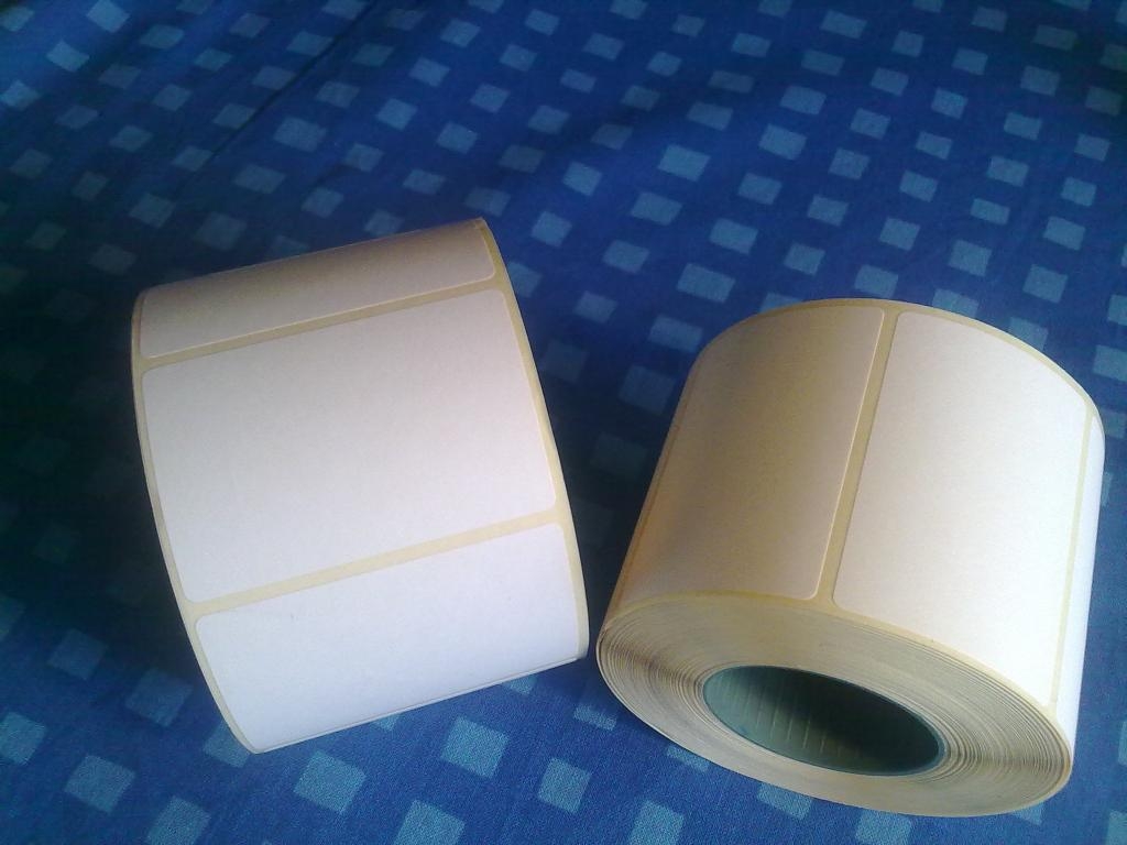 Dwie rolki białych etykiet samoprzylepnych na niebieskim tle z geometrycznym wzorem, gotowe do zadruku.