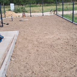 Domi-Rem - Przygotowany teren pod trawnik z widocznym ogrodzeniem panelowym i elementami instalacji. Widoczne narzędzia i materiały budowlane.