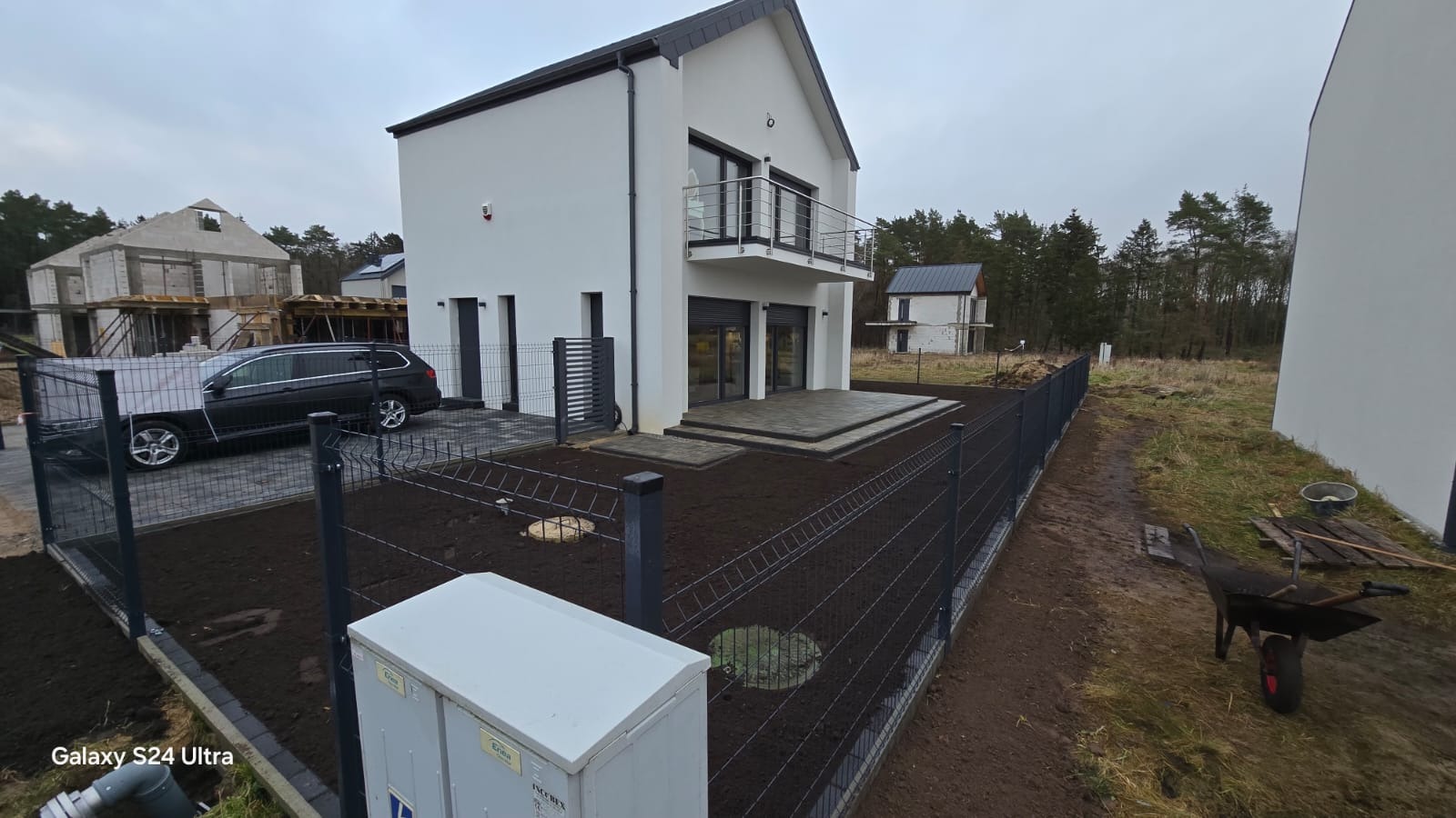 Nowoczesny dom jednorodzinny z szarym ogrodzeniem panelowym w Kamieniu Pomorskim. Widoczny świeżo obsadzony trawnik i fragment tarasu.