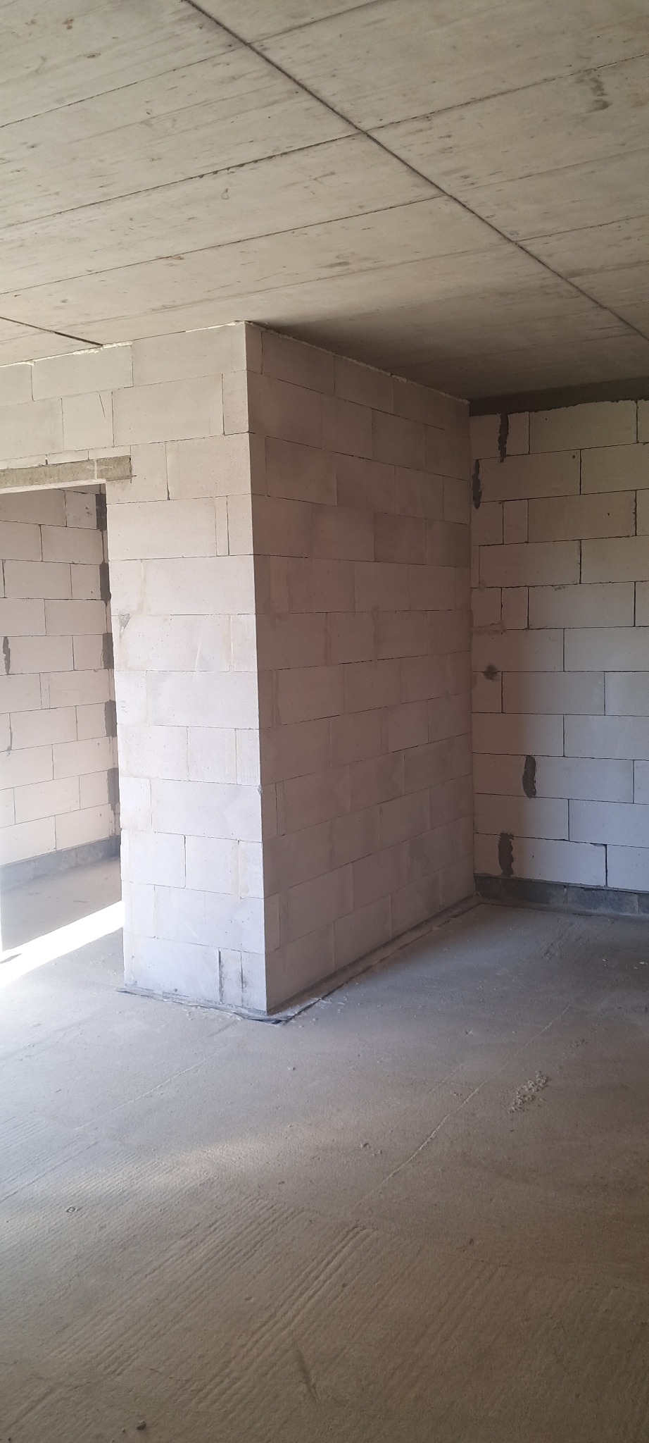 Wnętrze w trakcie budowy: surowy betonowy sufit, ściany z białych bloczków, widoczne spoiny. Minimalistyczny, industrialny klimat. Wnętrze do wykończenia.