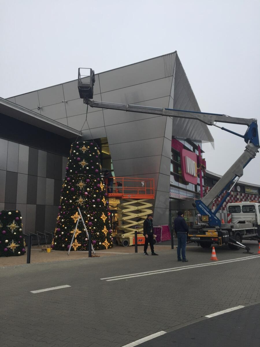 Montaż świątecznej dekoracji na zewnątrz budynku w Pysznicy przy użyciu podnośnika koszowego, widoczna choinka ozdobiona gwiazdami i bombkami.