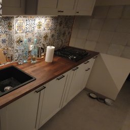 FMBUD - Nowoczesna kuchnia z ciemnym blatem, białymi szafkami z czarnymi uchwytami, kolorową mozaiką nad blatem, czarnym zlewem i płytą gazową.