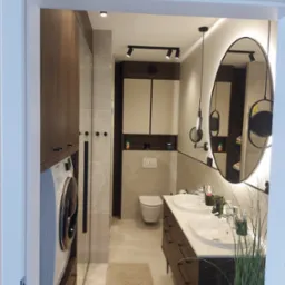Nowoczesna łazienka z pralką w zabudowie, podwójną umywalką, owalnym lustrem z podświetleniem LED i minimalistycznym oświetleniem punktowym.
