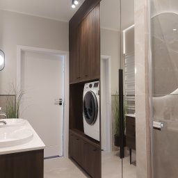 M-Bud Marek Kujawa - Nowoczesna łazienka z zabudową z ciemnego drewna, w której umieszczono pralkę. Umywalka z białym blatem i duże lustro optycznie powiększają przestrzeń.