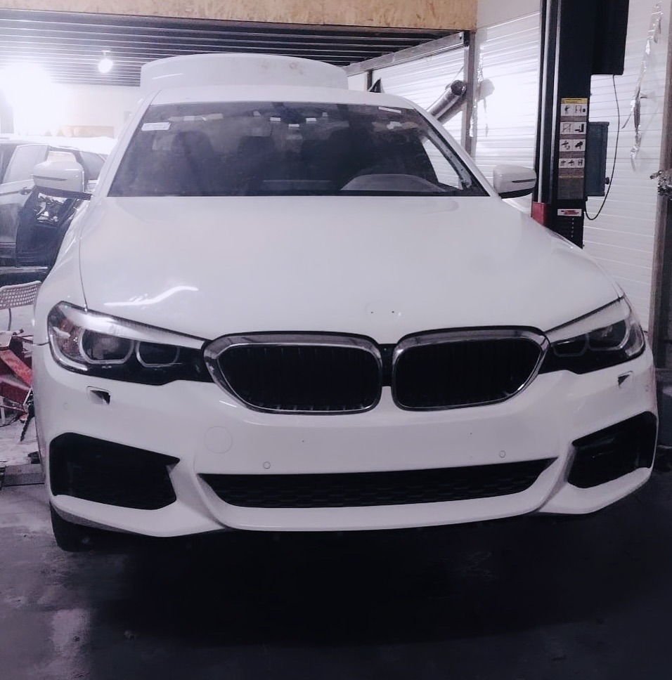 Biały samochód marki BMW na podnośniku w warsztacie, z widoczną maską zabezpieczoną folią.