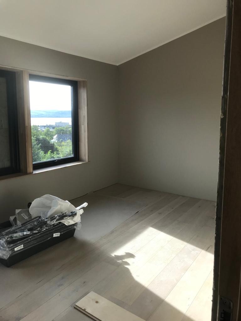 Jasne panele ułożone we wzór jodełki w słonecznym pokoju, widoczne narzędzia w pojemniku i fragmenty paneli do ułożenia.