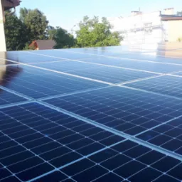 Błyszczące panele słoneczne na dachu budynku w słoneczny dzień, odbijające niebo i otoczenie.