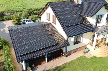 Dom jednorodzinny z panelami słonecznymi na dachu, widok z góry, w tle zaparkowany samochód.