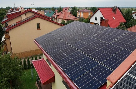 Instalacja paneli słonecznych na dachu domu jednorodzinnego z czerwonym dachem, widok z góry na osiedle domów.