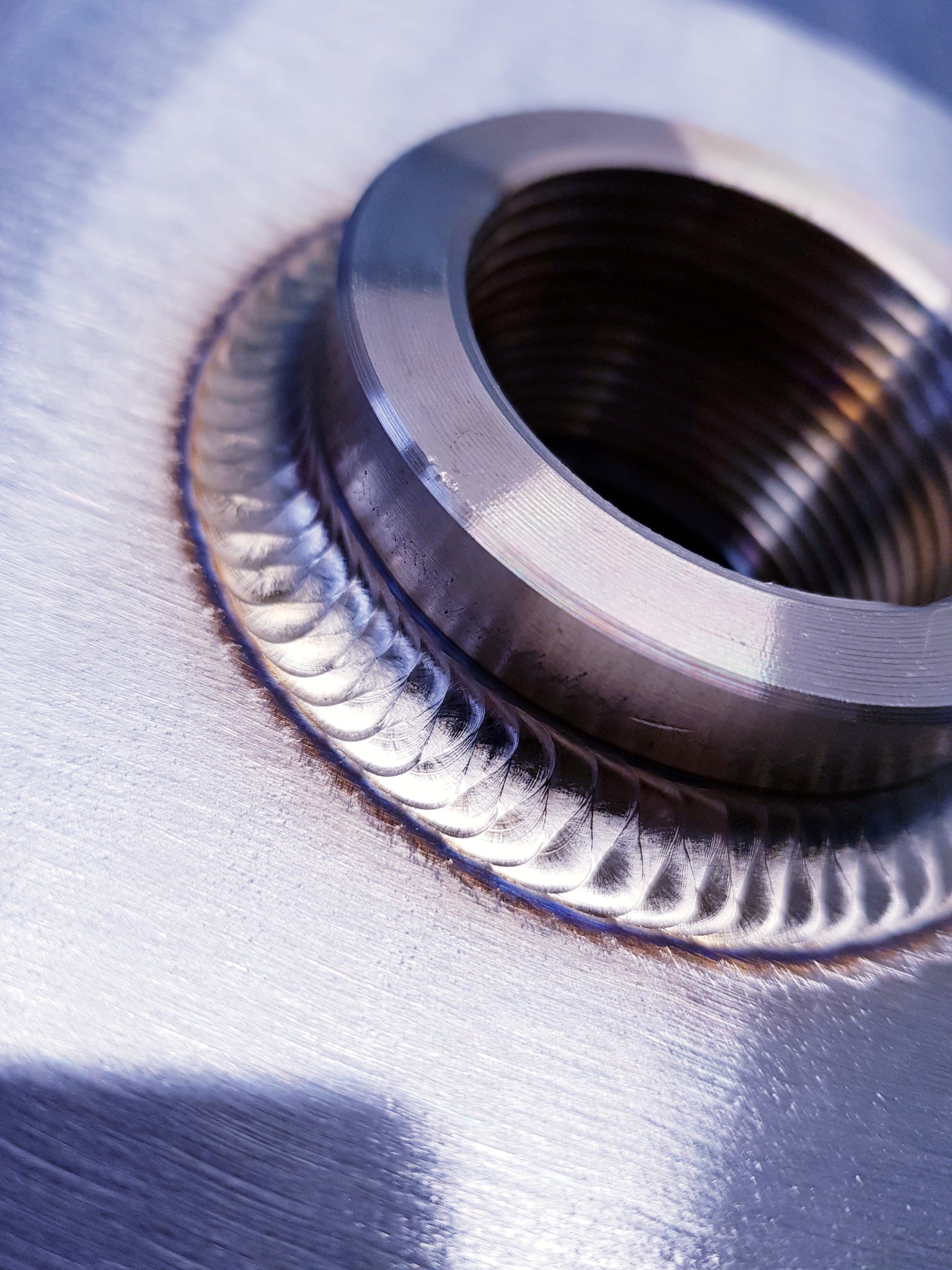 Szczegółowe zbliżenie spawu pierścienia z gwintem do metalowej powierzchni, widoczne ślady obróbki i regularny wzór spoiny.