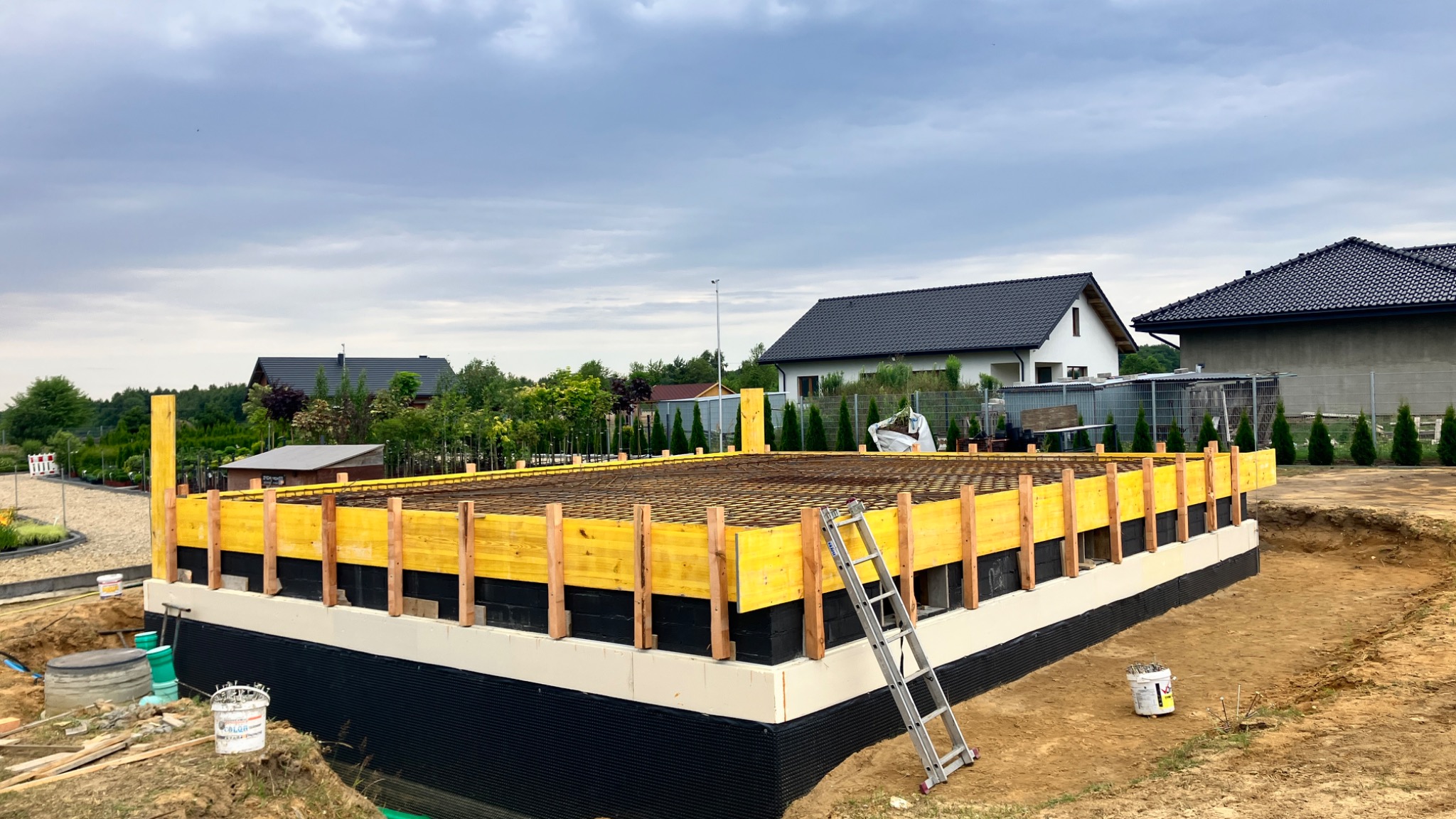 Zbrojony fundament domu jednorodzinnego z deskowaniem i izolacją przeciwwilgociową, widoczna drabina oparta o deskowanie.