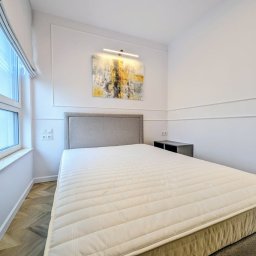 OnyxArt Piotr Padowski - Nowoczesna sypialnia z łóżkiem kontynentalnym, szarym zagłówkiem, abstrakcyjnym obrazem w złoto-czarnych tonacjach i parkietem ułożonym we wzór jodełki.