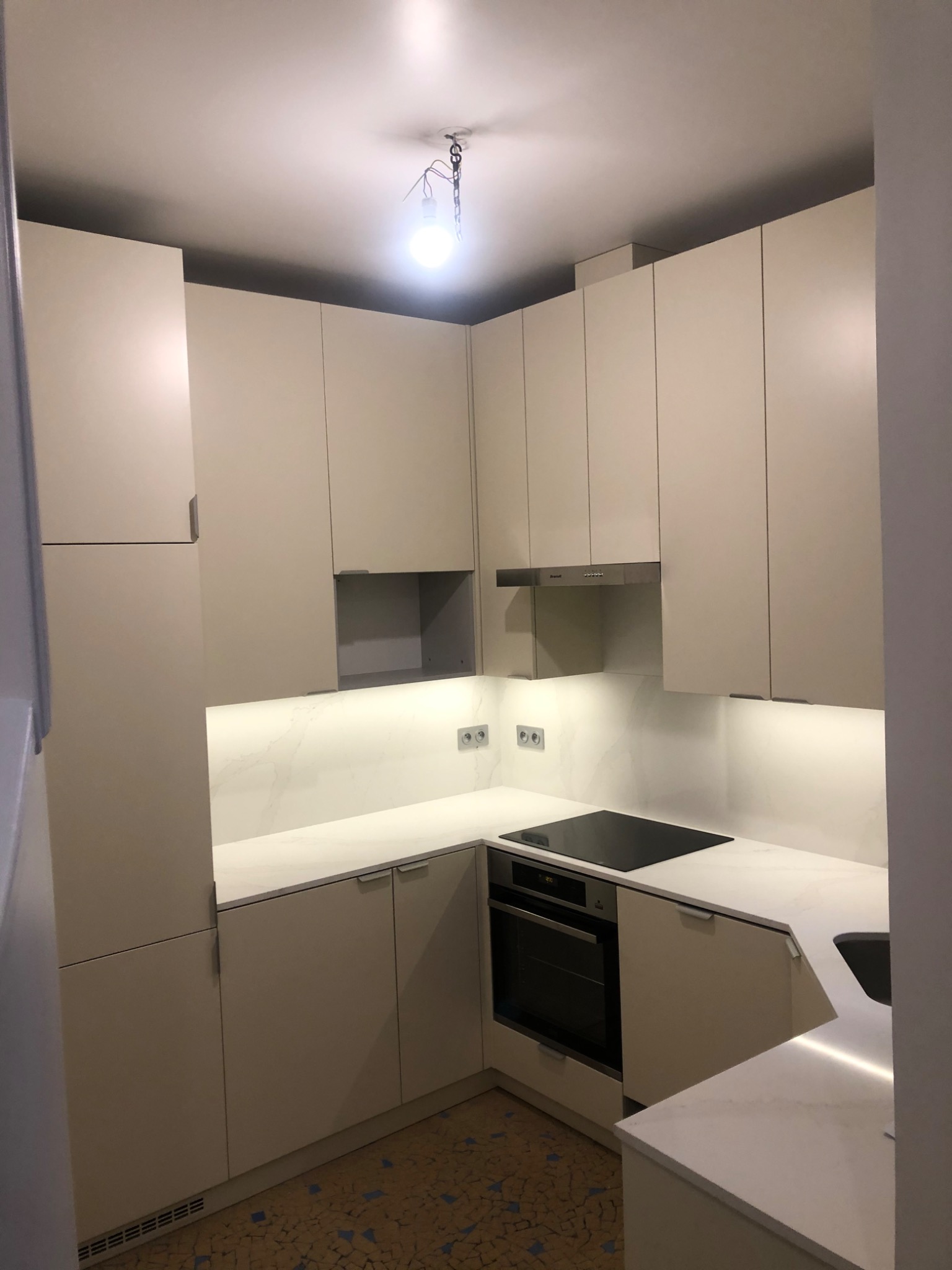 Jasna, nowoczesna kuchnia w Rzeszowie z zabudową meblową pod sufit, oświetleniem LED pod szafkami wiszącymi i płytą indukcyjną, widok na fragment mozaikowej podłogi.