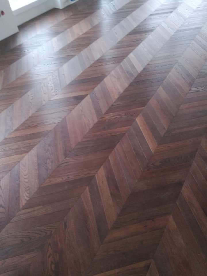 Ułożony parkiet w jodełkę w odcieniach brązu, widoczne słoje drewna i subtelne różnice w kolorze poszczególnych klepek.