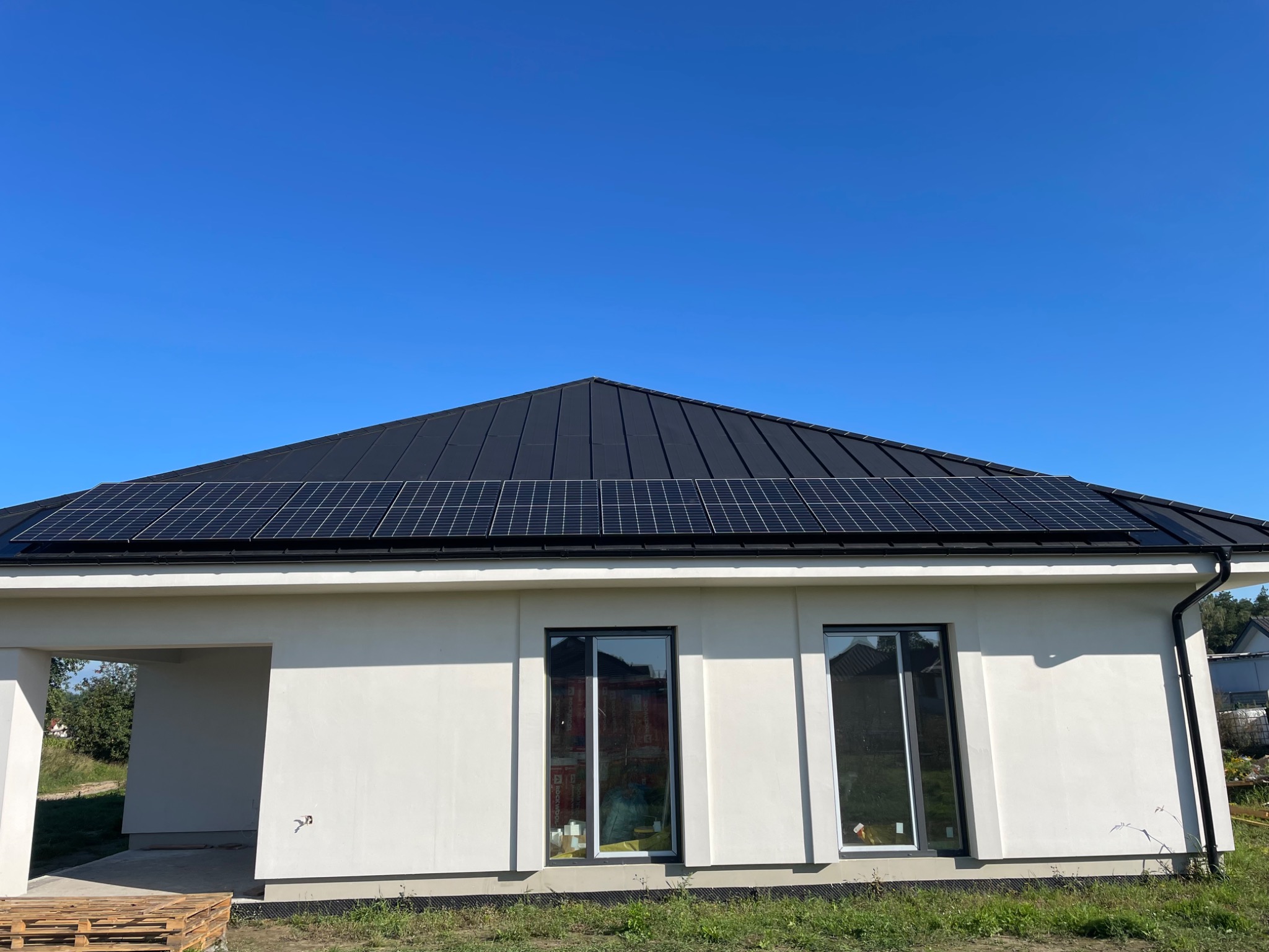 Nowoczesny dom jednorodzinny z czarnym dachem i panelami słonecznymi w słoneczny dzień, widok z poziomu gruntu.