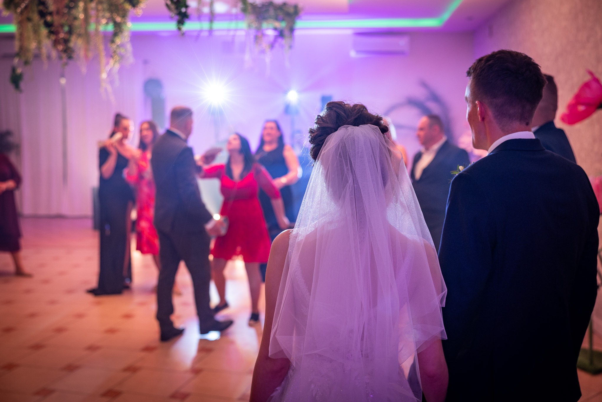 Para młoda na parkiecie podczas wesela, w tle goście bawiący się w blasku świateł.