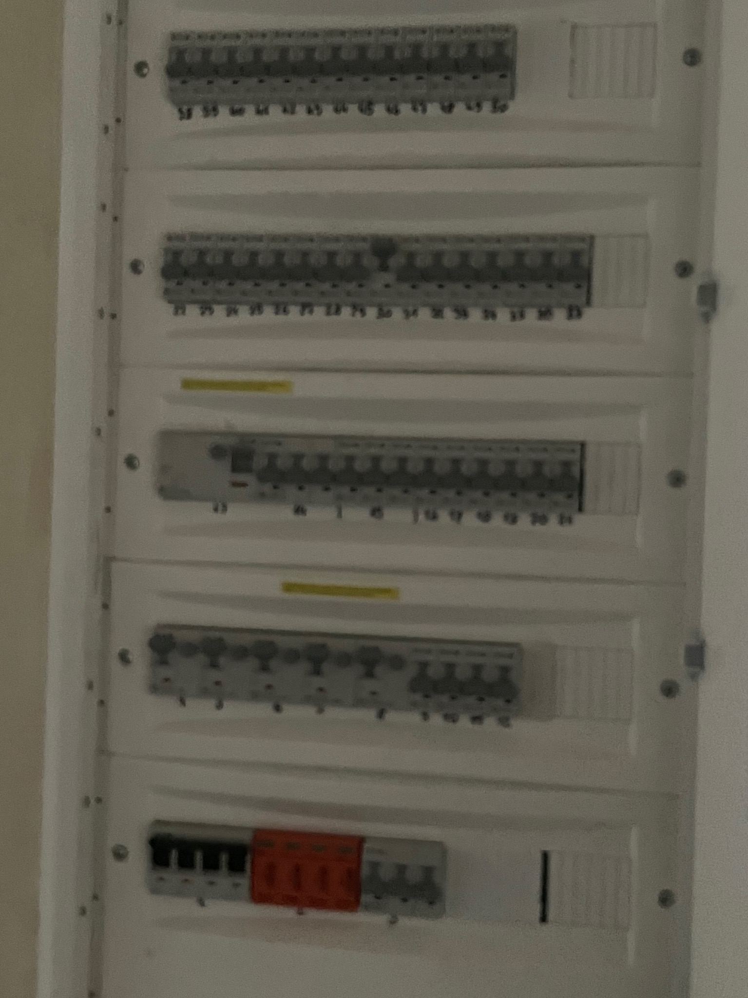 Rozdzielnica elektryczna z bezpiecznikami i wyłącznikami różnicowoprądowymi, widok od frontu, na białej ścianie.