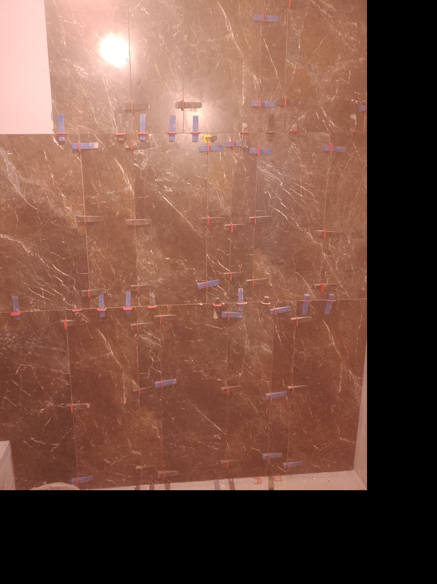 Brązowe płytki imitujące marmur, ułożone na ścianie z użyciem systemu poziomowania płytek (klipsy i kliny).