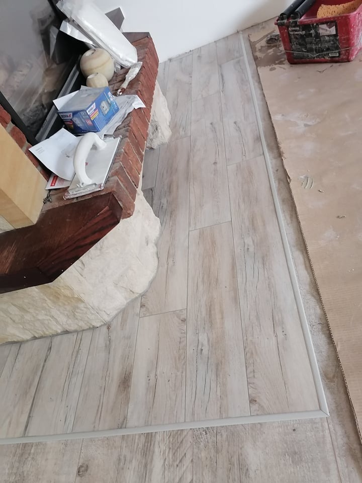 Ułożona podłoga z paneli imitujących drewno, widoczny fragment kominka z kamienia, narzędzia i akcesoria budowlane na podłodze zabezpieczonej kartonem.