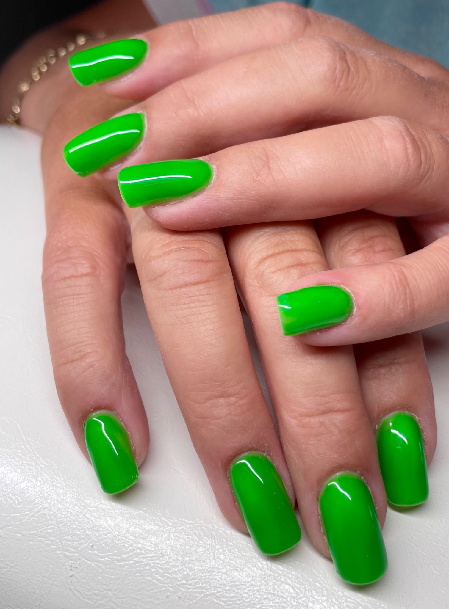 Dłonie z jaskrawozielonymi, błyszczącymi paznokciami o zaokrąglonym kształcie, na białym tle.