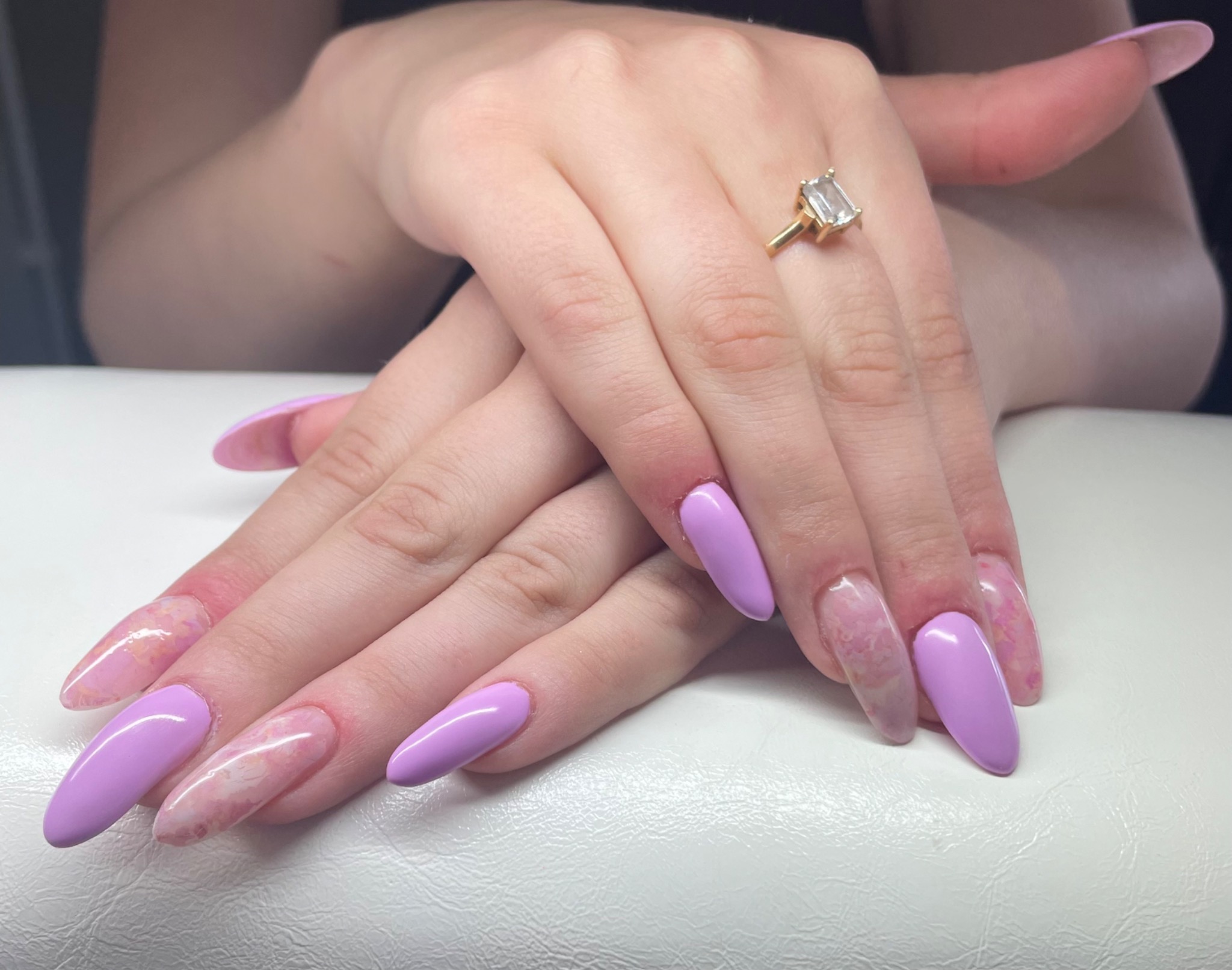 Dłonie ze świeżo wykonanym manicure w Bliżynie, z paznokciami w odcieniach lilii i marmurkowego różu, ozdobione złotym pierścionkiem z prostokątnym kamieniem.