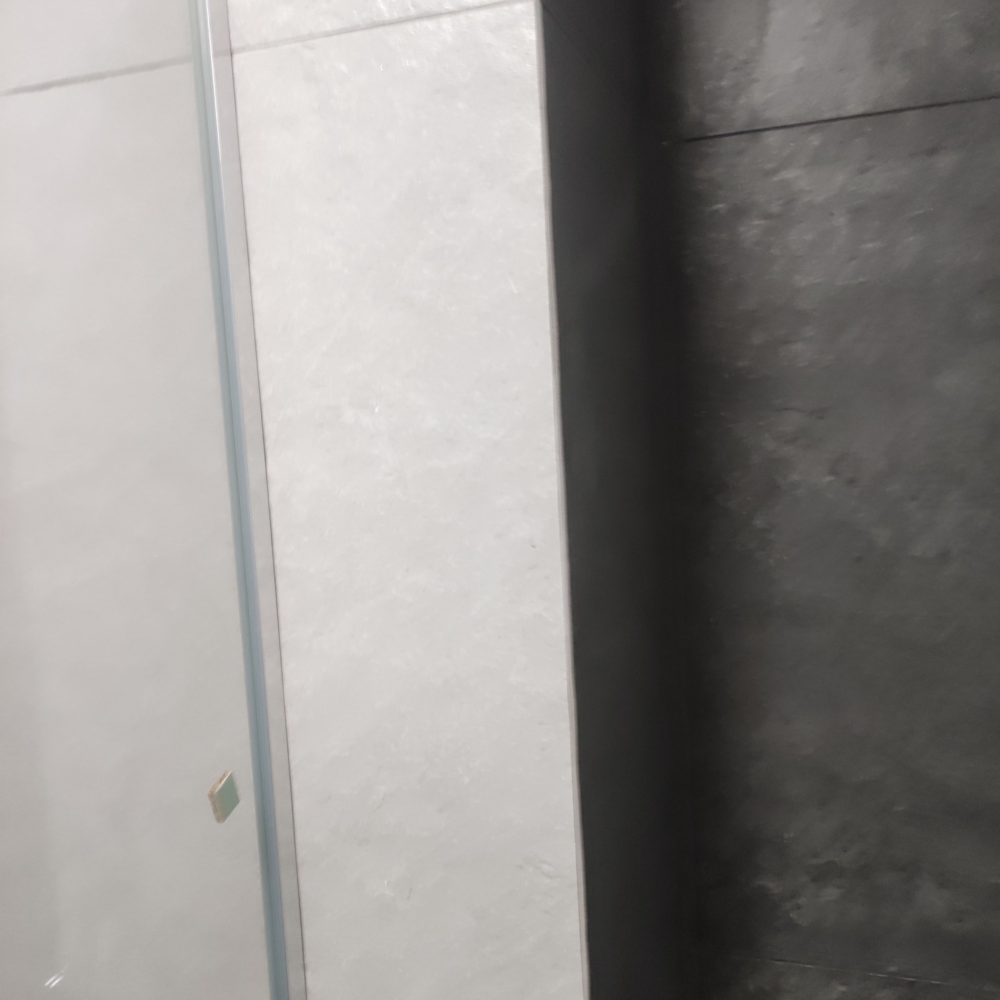 Fragment wykończonej łazienki z kabiną prysznicową z przezroczystego szkła i płytkami w odcieniach szarości i bieli.