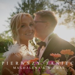 CINEMATOGRAPHY KONRAD GRADOWSKI - Uśmiechnięta panna młoda z bukietem, całowana w policzek przez pana młodego na tle zieleni i zachodzącego słońca. Napis: 'Pierwszy taniec Magdalena & Michał'.