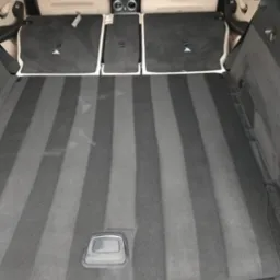 Wnętrze bagażnika samochodu po czyszczeniu, widoczne świeże pasy na dywaniku, jasne fotele skórzane w tle.