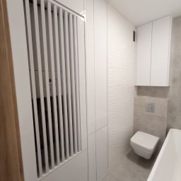 Piomax Piotr Kamiński - Biała szafa wnękowa z lamelami maskującymi licznik w łazience w Kościerzynie, dopasowana do minimalistycznego wystroju z sanitariatami w tle.