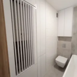 Biała szafa wnękowa z lamelami maskującymi licznik w łazience w Kościerzynie, dopasowana do minimalistycznego wystroju z sanitariatami w tle.