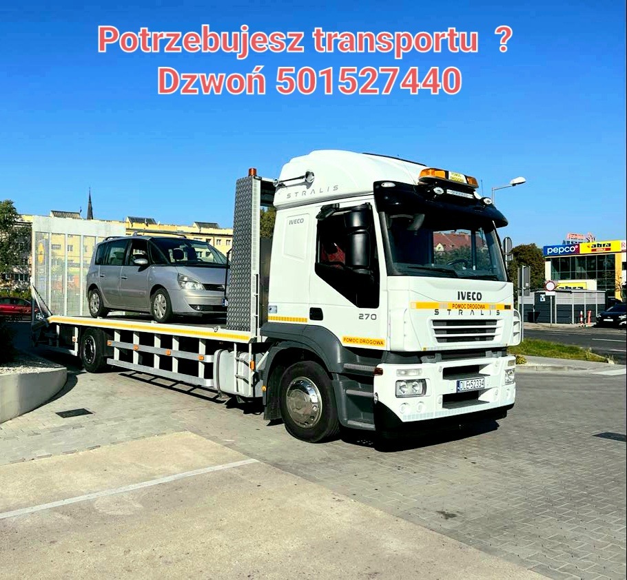 Biała laweta Iveco Stralis z załadowanym srebrnym minivanem Renault Espace, widoczny numer telefonu kontaktowego na górze zdjęcia.