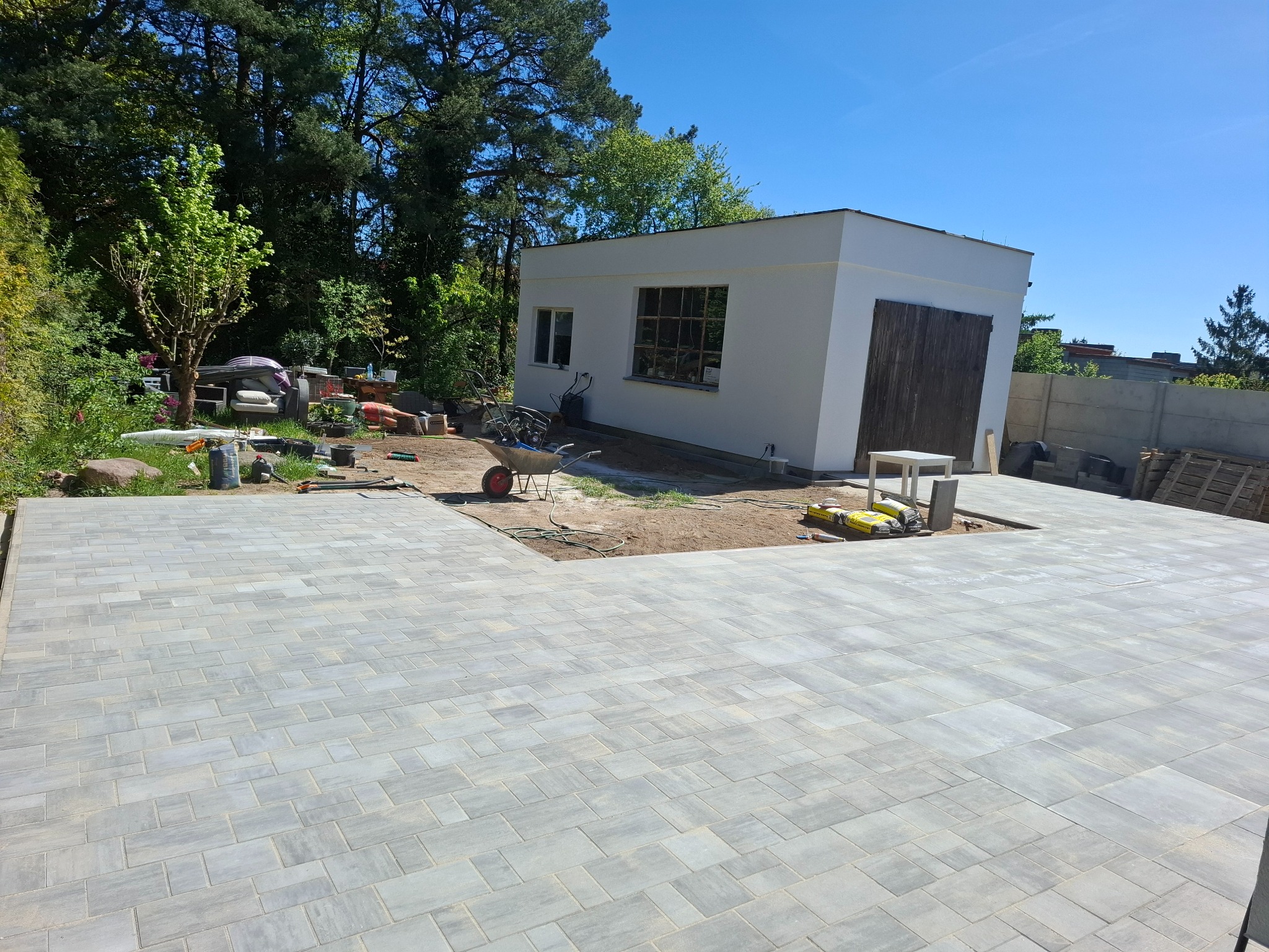 Jasnoszara kostka brukowa ułożona na posesji, widoczny budynek gospodarczy i przygotowany teren pod dalsze prace. Słoneczny dzień, wyraźne detale kostki.