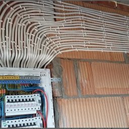 Oleg Vahniuk - Rozdzielnica elektryczna z licznymi przewodami ułożonymi równolegle i przymocowanymi do surowej ściany z cegły dziurawki.