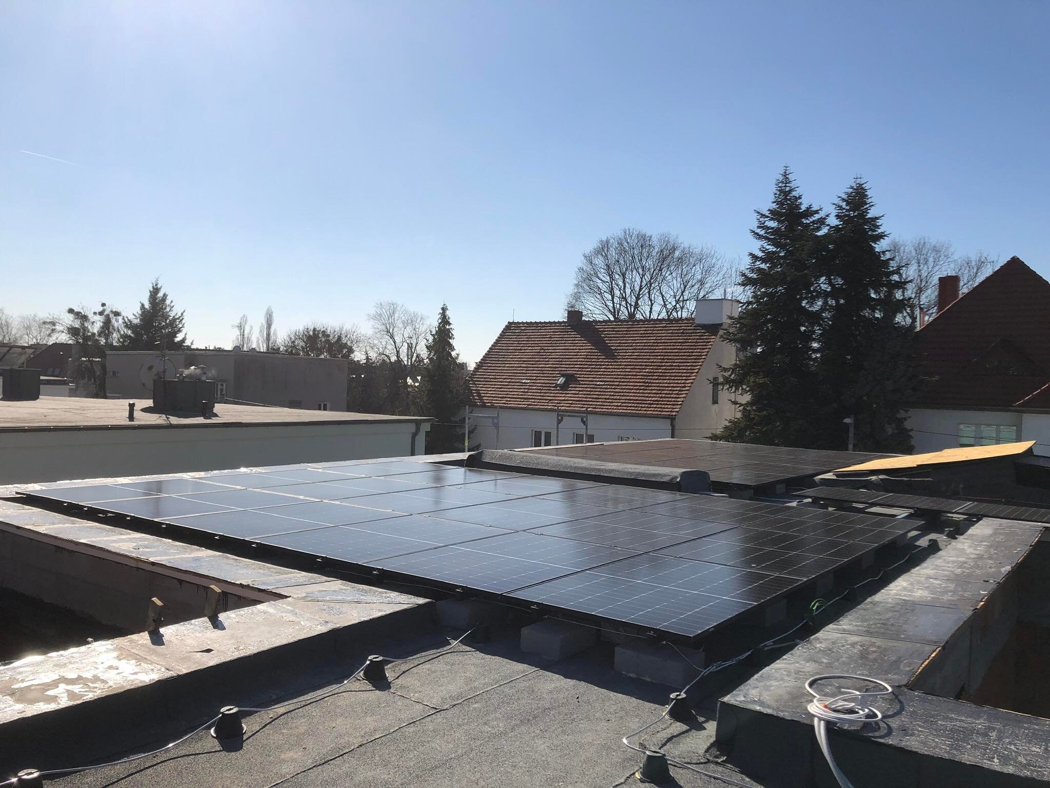 Panel słoneczny na dachu budynku mieszkalnego w słoneczny dzień, widoczne elementy montażowe i przewody.